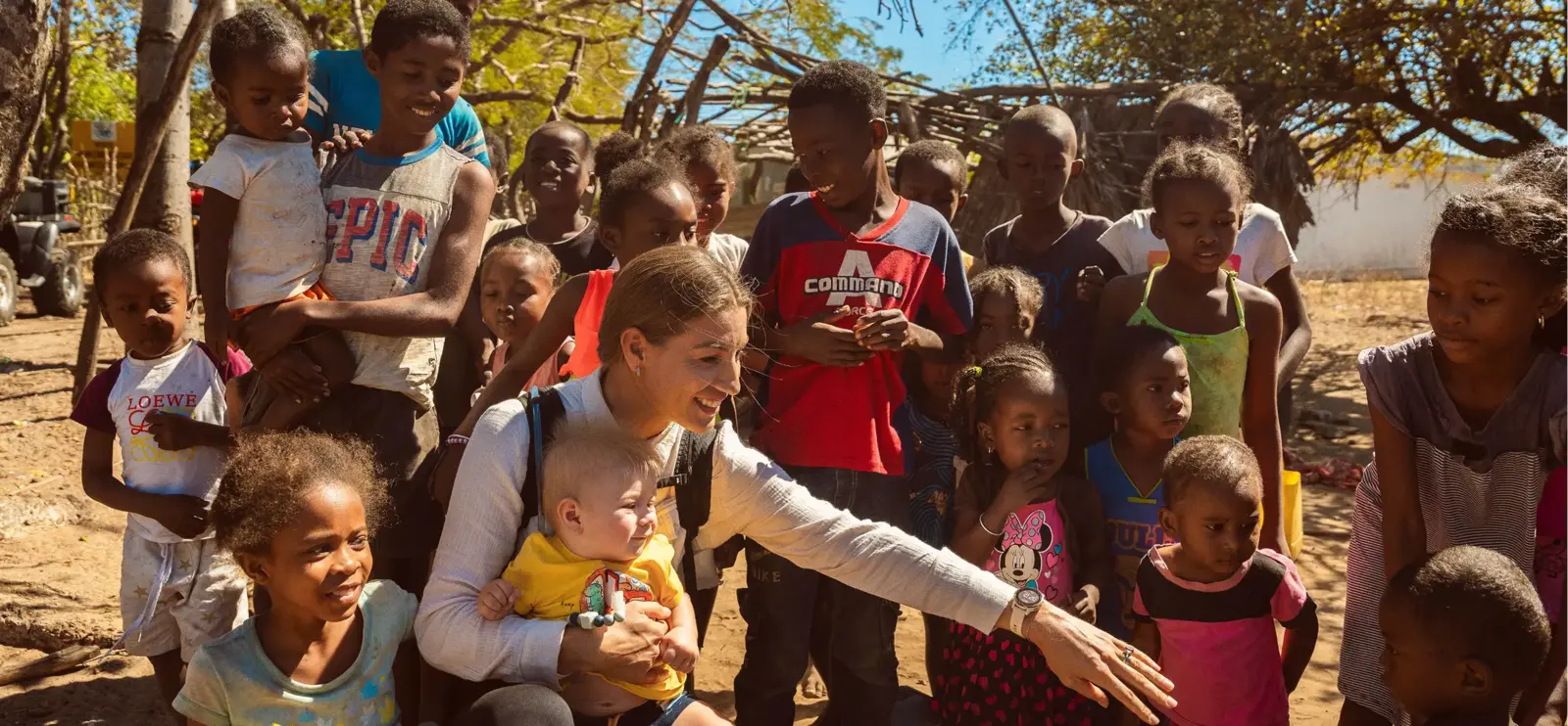 A woman joyfully interacts with children in a dirt field